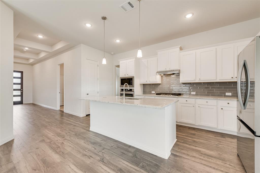 Kitchen featuring a center island with a stone-finish countertop, white cabinetry, a gray tiled backsplash, built-in stainless steel double ovens, and wood-finish flooring