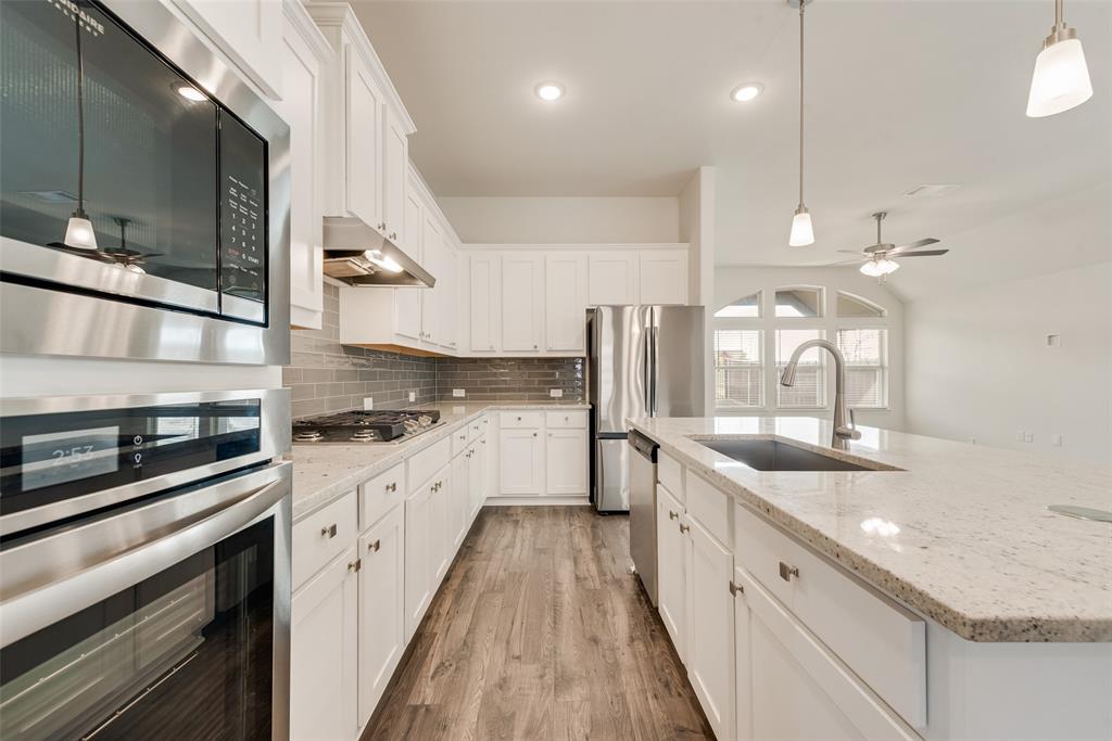 Kitchen featuring white shaker cabinetry, stone-finish countertops, stainless steel appliances including a built-in wall oven and microwave, gray subway tile backsplash, and wood-finish flooring