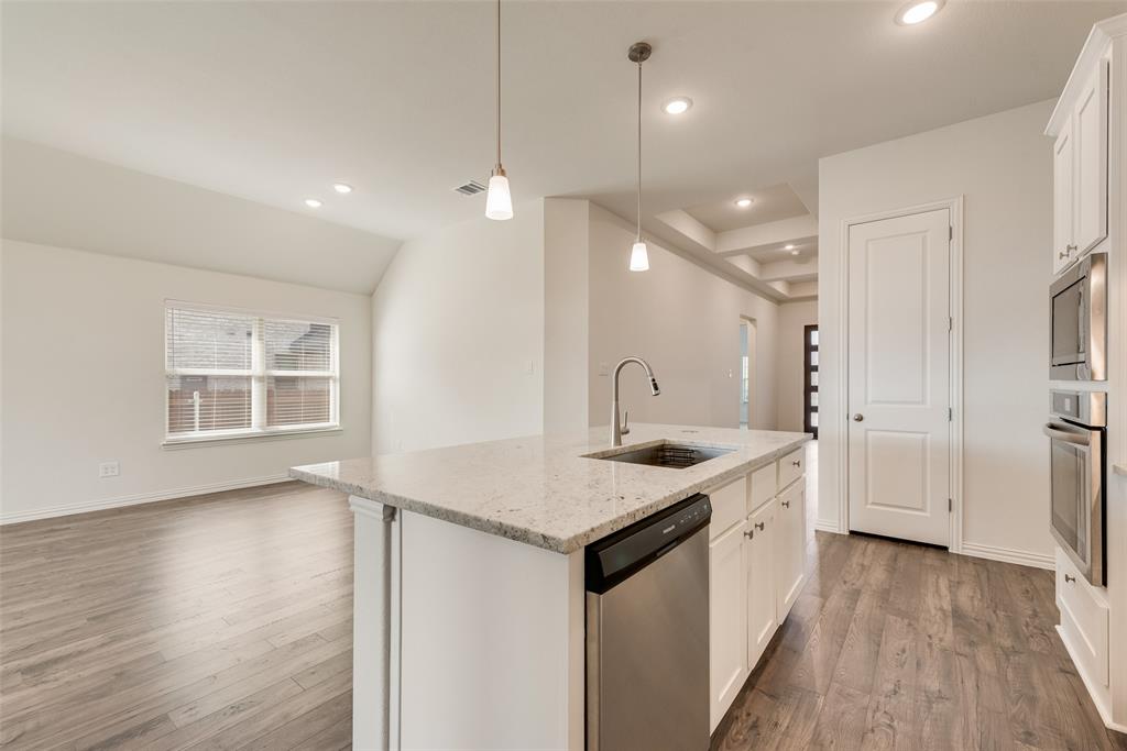 Kitchen island featuring stone countertops, integrated stainless steel sink, wood-finish flooring, recessed lighting, and built-in stainless steel double wall ovens