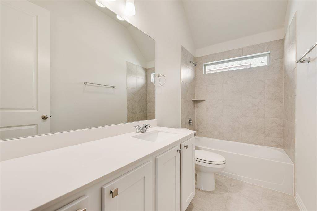 Vanity with a solid surface countertop, rectangular under-mount sink, oversized wall mirror, vaulted ceiling, and a porcelain tile shower surround with integrated shelving