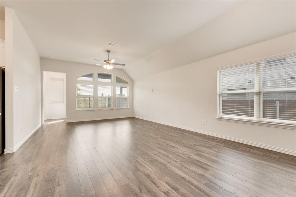 Open-concept interior featuring wood-finish flooring, vaulted ceilings, a multi-pane arched window, and a ceiling fan with integrated lighting