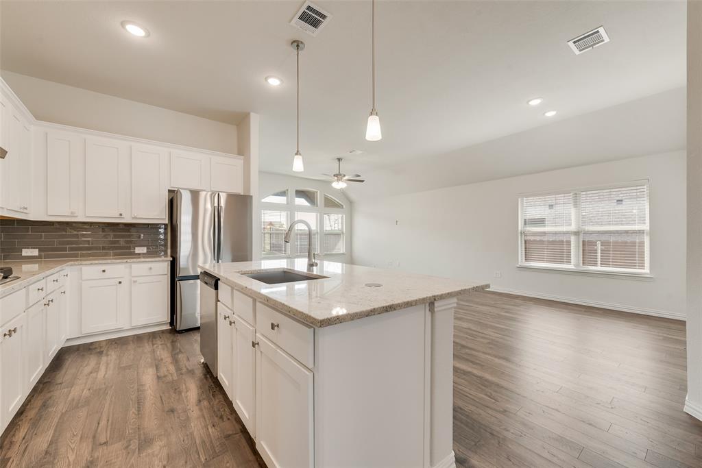 Kitchen featuring white cabinetry, stone-surface island with integrated sink, stainless steel refrigerator, tile backsplash, and wood-finish flooring