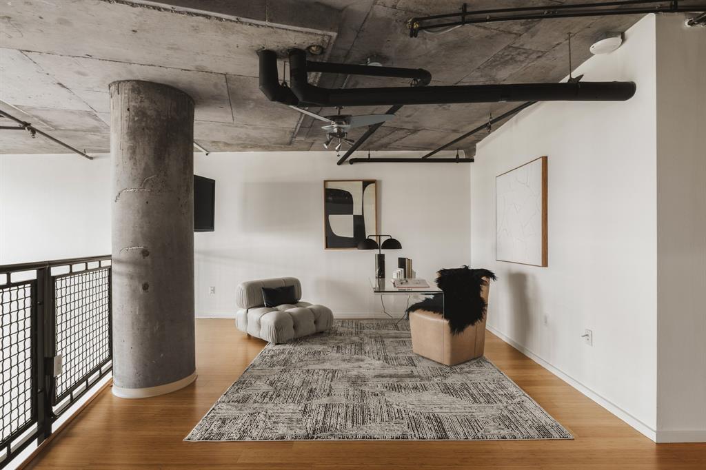 Exposed concrete ceiling, industrial-style black piping, concrete structural column, light wood-finish flooring, and white painted walls