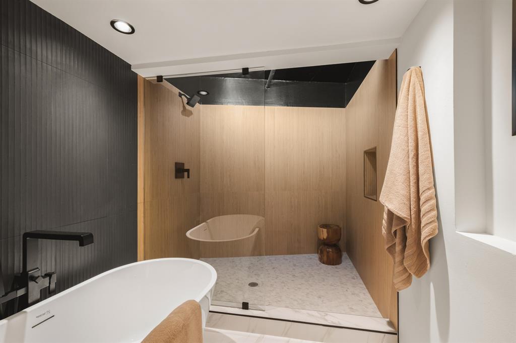 Freestanding soaking tub with a wall-mounted matte black faucet, walk-in shower with light wood-finish walls, glass enclosure, and recessed lighting