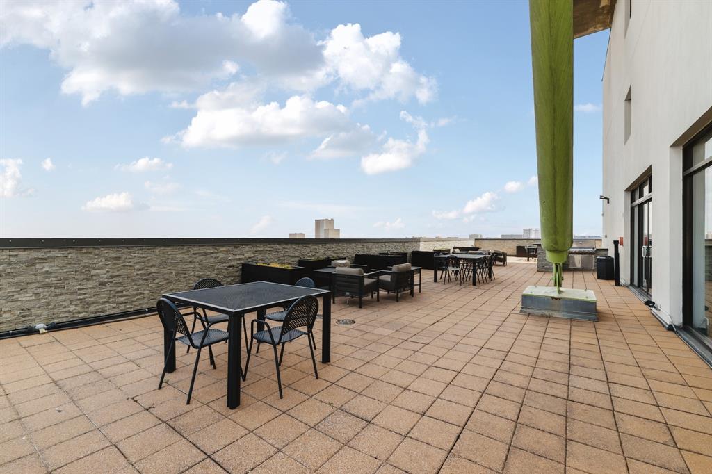 Expansive outdoor terrace featuring paver flooring, a perimeter wall, and a building exterior with large window openings