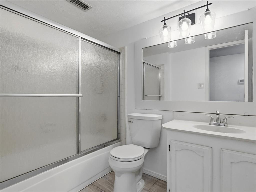 Bathroom featuring a vanity with integrated sink, full-width mirror, three-light fixture, and tub with a sliding glass enclosure