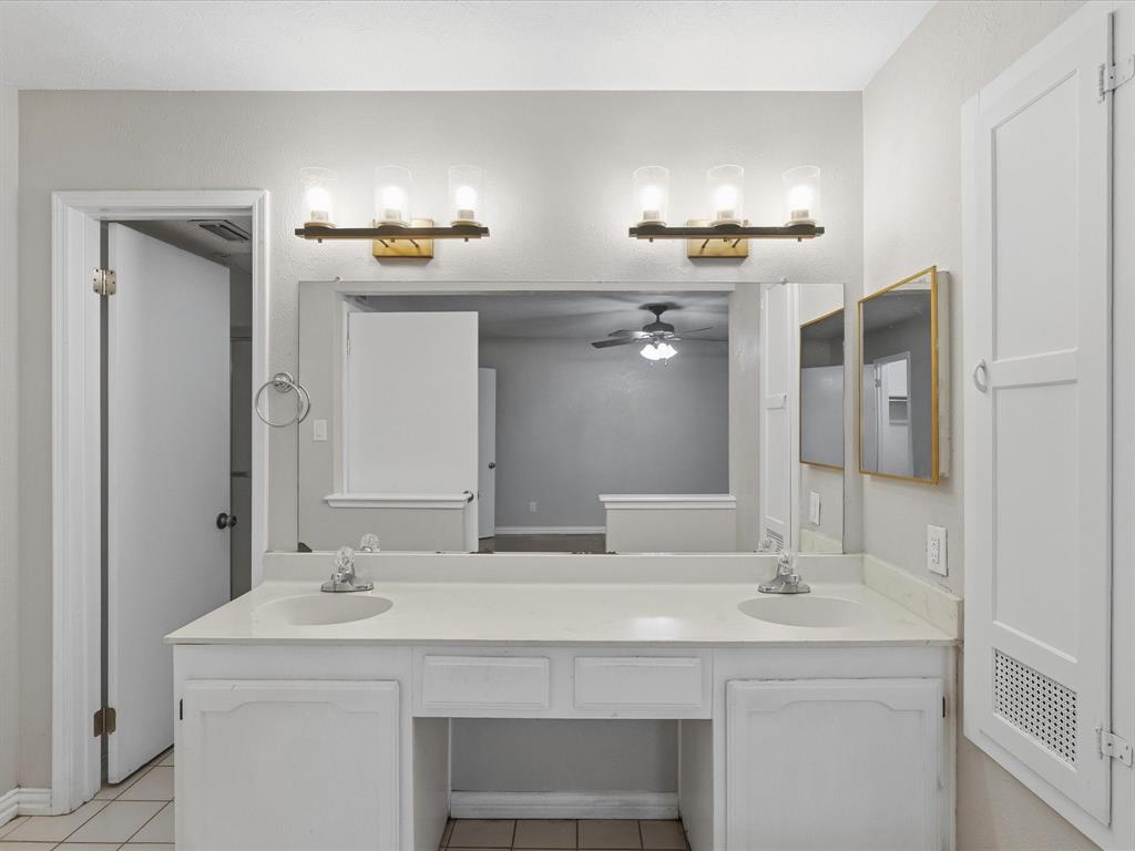Double vanity featuring white cabinetry, a light-toned solid surface countertop with integrated dual sinks, two three-light fixtures, and a large plate glass mirror
