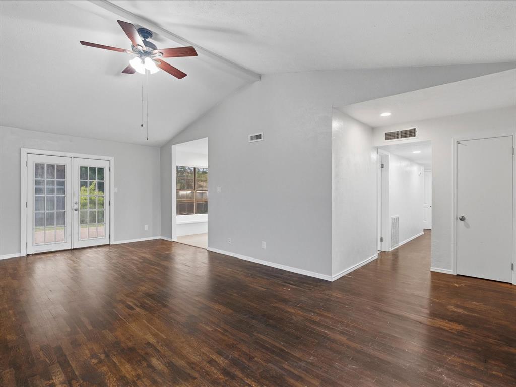 Vaulted ceiling featuring a central ceiling fan with multi-light fixture, wood-finish flooring, and glass-paneled double doors