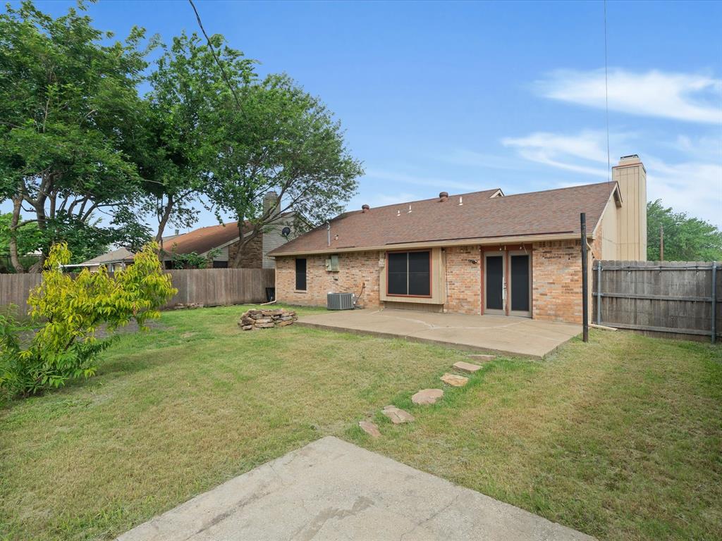 Backyard featuring a concrete patio, stone stepping path, brick exterior, chimney, and wood perimeter fencing