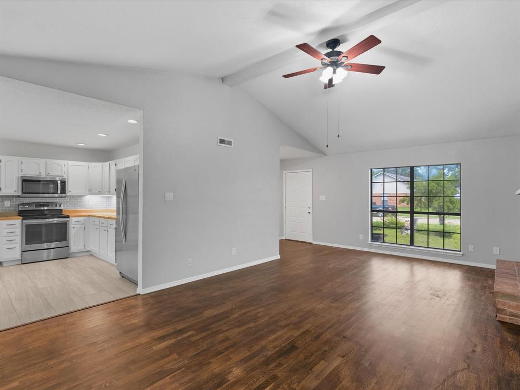 Open-concept room featuring vaulted ceilings, dark wood-finish flooring, a ceiling fan with integrated lighting, and a grid-pane window