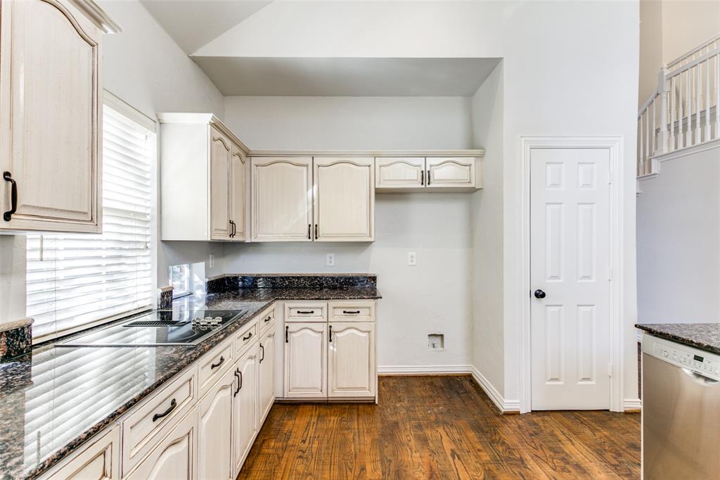 Kitchen featuring vaulted ceilings, wood-finish flooring, dark stone countertops, off-white cabinetry with matte black hardware, and stainless steel integrated dishwasher