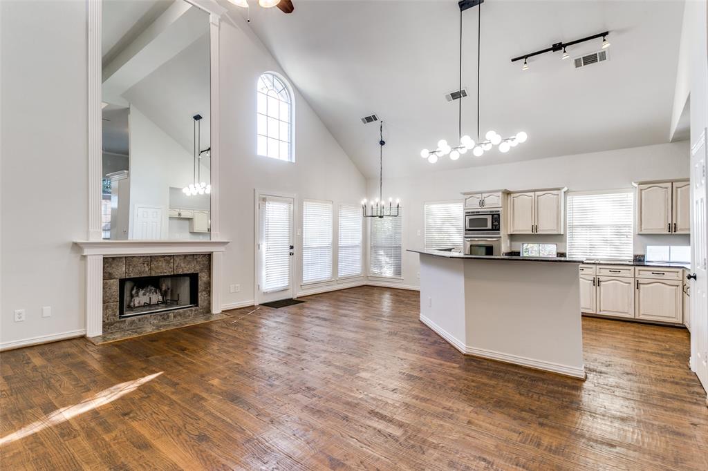 Vaulted ceilings, wood-finish flooring, stone-surround fireplace with floor-to-ceiling mirror, arched window, and custom kitchen cabinetry with integrated stainless steel appliances