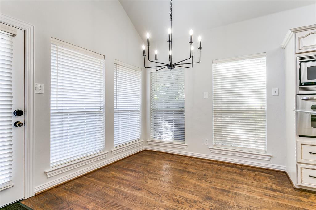 Vaulted ceiling featuring a multi-arm iron chandelier, wood-finish flooring, and multiple windows with horizontal blinds