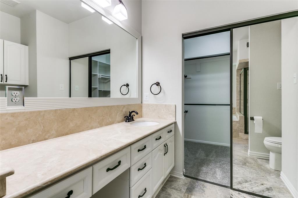 Vanity featuring a stone countertop with an integrated basin, white cabinetry with dark hardware, a full-width mirror, and a sliding glass door