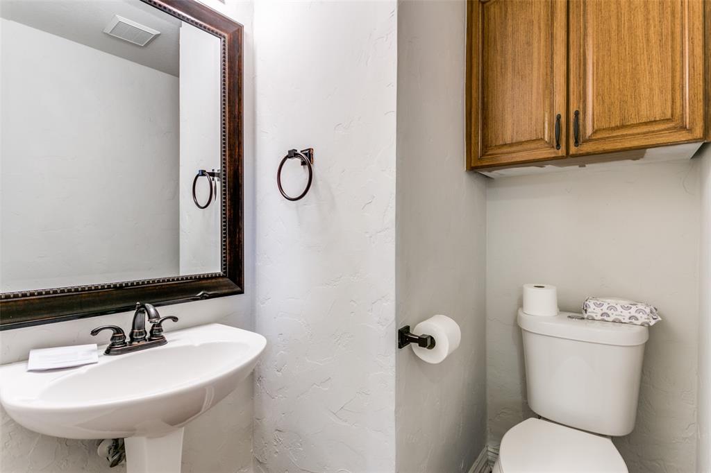Wall-mounted wood-finish cabinetry, pedestal sink with dual-handle metal faucet, and framed wall mirror with coordinating metal hardware