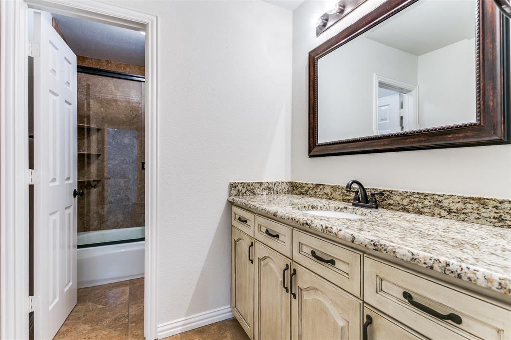 Bathroom featuring stone-surface vanity with undermount sink, oil-rubbed bronze faucet, custom cabinetry with dark hardware, and a tile-surround shower with built-in shelving