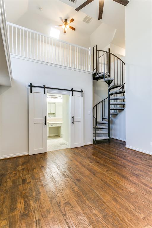 Vaulted ceilings featuring a black metal spiral staircase, wood-finish flooring, white sliding barn doors with matte black hardware, and an open balcony with a white railing