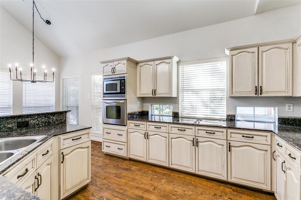 Kitchen featuring wood-finish flooring, stone countertops, double wall ovens, cabinetry with arched-panel detailing, and a vaulted ceiling with an iron chandelier