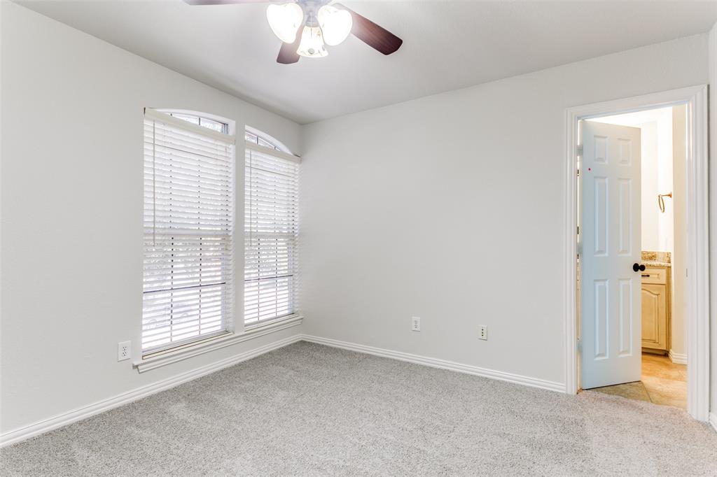 Neutral interior space featuring arched windows, wall-to-wall carpeting, and a ceiling fan with integrated lighting