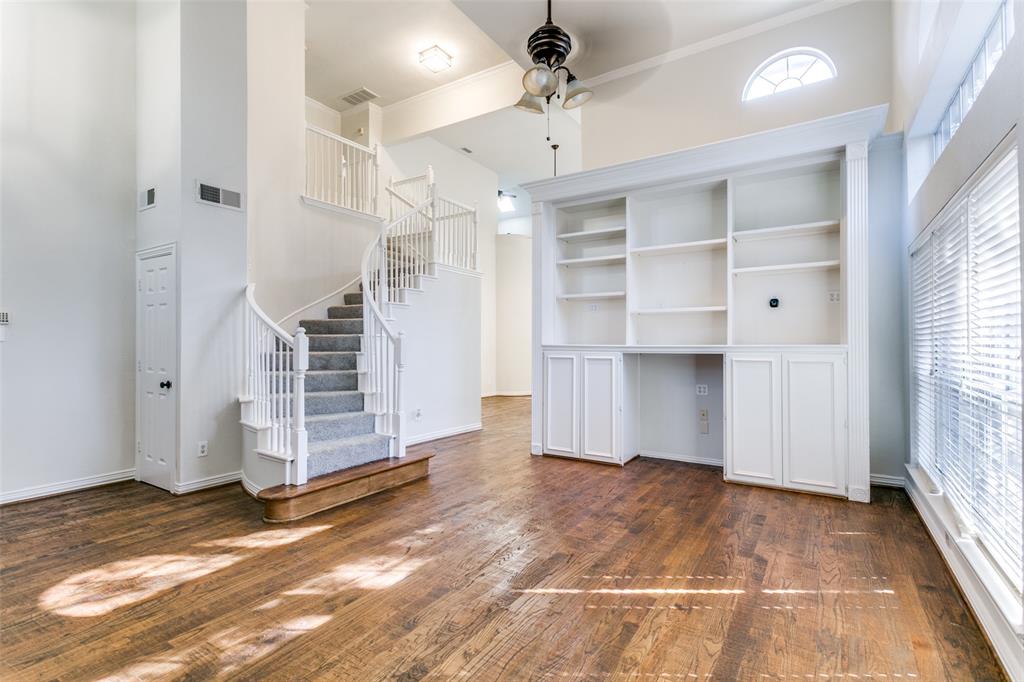 Living area featuring wood-finish flooring, a vaulted ceiling, a built-in floor-to-ceiling white bookshelf with cabinetry, a curved staircase with white railings, and an arched transom window