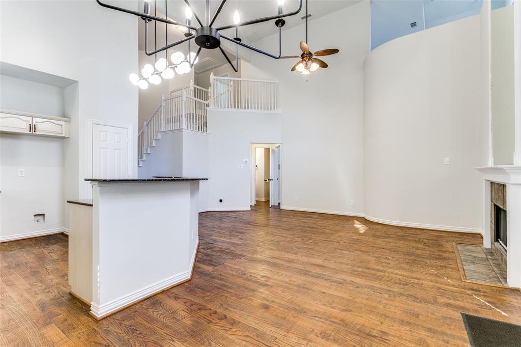 Open concept living area featuring vaulted ceilings, wood-finish flooring, a tiered staircase with white balusters, a built-in fireplace with stone hearth, and a multi-light chandelier
