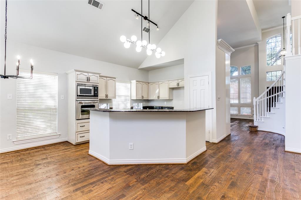 Kitchen featuring wood-finish flooring, vaulted ceilings, stone-surfaced island countertop, built-in wall oven and microwave, and multi-light chandelier