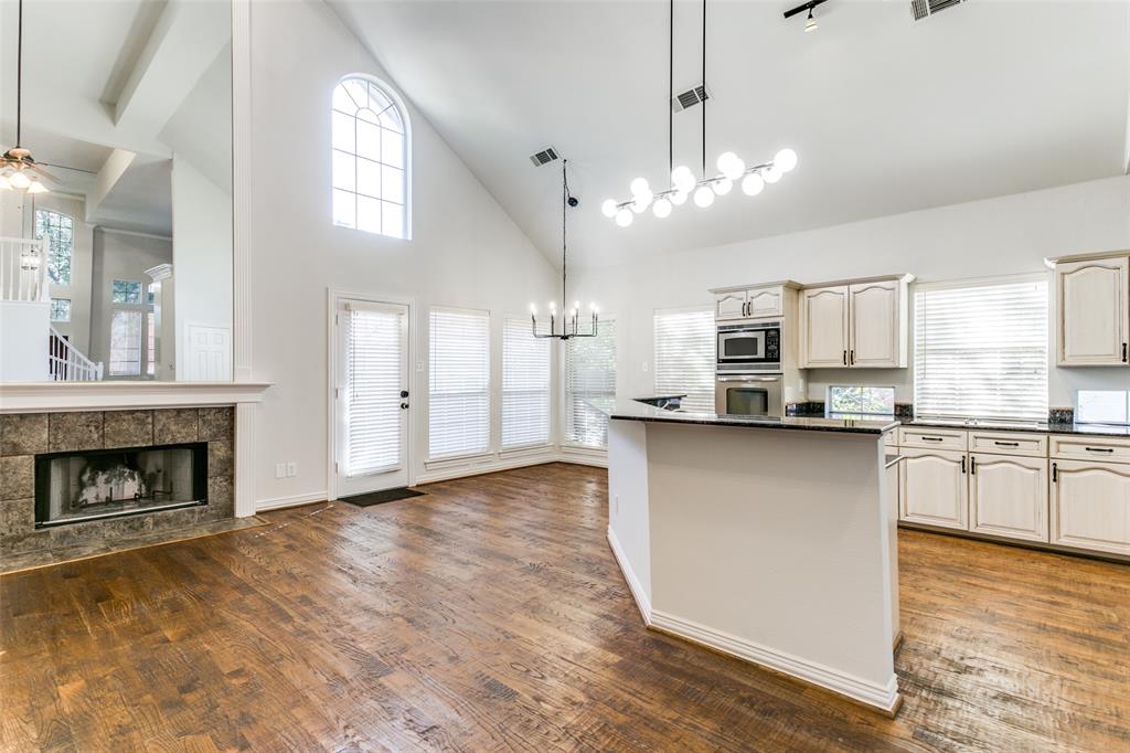 Vaulted ceilings, wood-finish flooring, stone-surround fireplace, multi-light chandeliers, and cabinetry with integrated stainless steel appliances