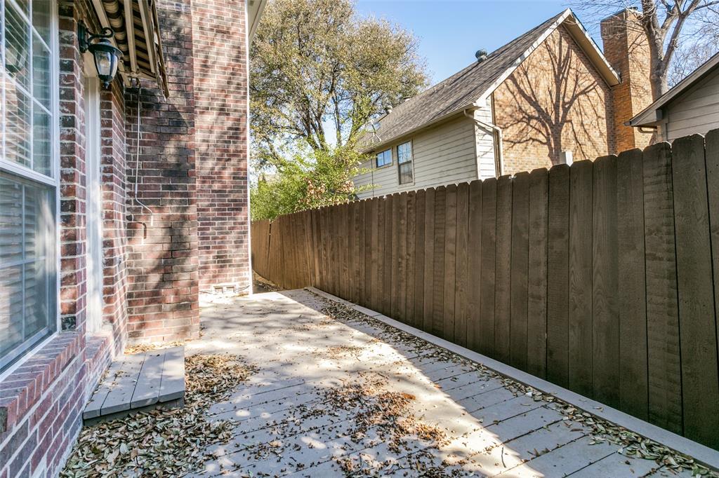 Exterior side yard featuring a brick facade, concrete patio, and vertical wood fencing