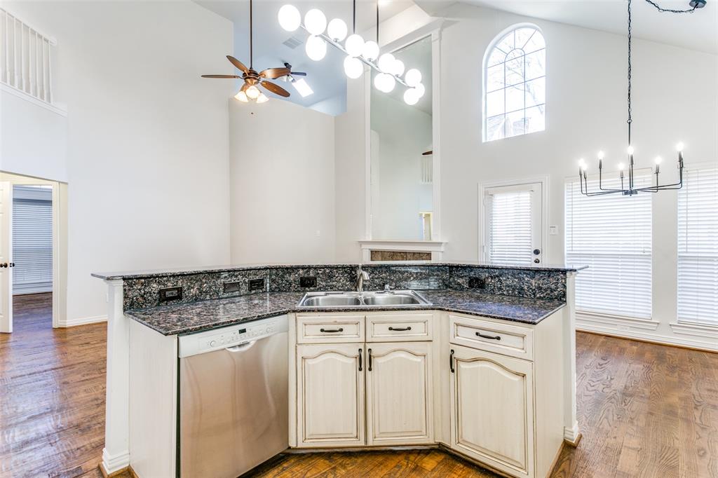 Kitchen featuring an island with stone-finish countertops, stainless steel dishwasher, double basin undermount sink, and light-toned cabinetry, accented by dual overhead chandeliers and vaulted ceilings