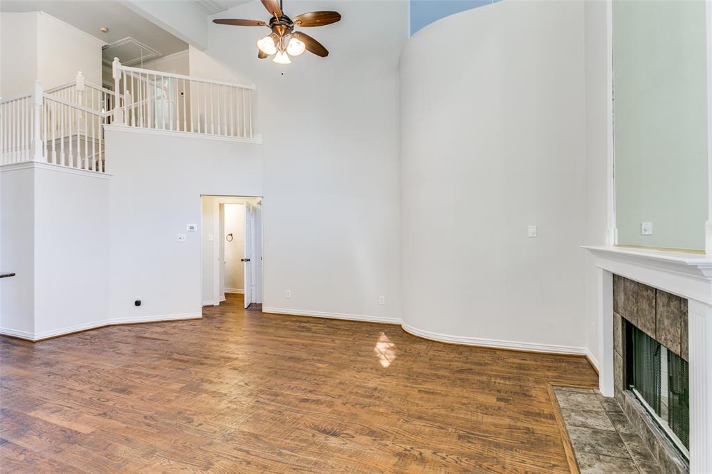 High-ceiling interior featuring wood-finish flooring, a curved architectural wall, a fireplace with tile surround, and an elevated balustrade landing