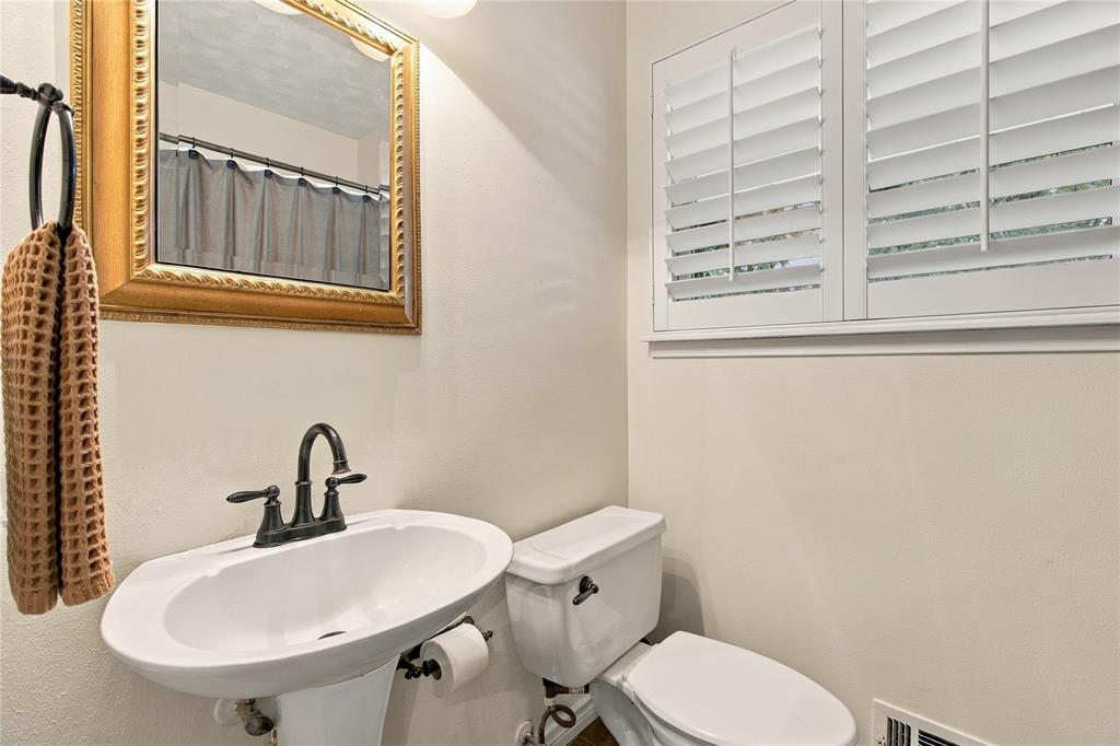 Pedestal sink with an oil-rubbed bronze faucet, decorative gold-toned framed mirror, and white plantation shutters