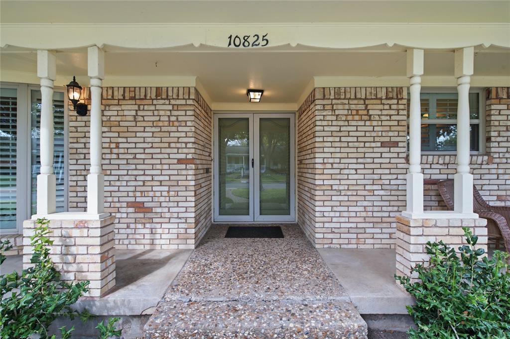Covered front porch featuring light brick masonry, decorative turned wood columns, aggregate concrete flooring, and a double-glass entry door Covered front porch featuring light brick masonry, decorative turned wood columns, aggregate concrete flooring, and a double-glass entry door