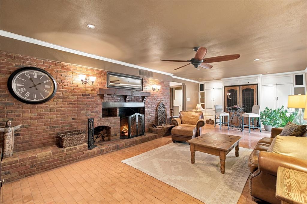 Exposed brick fireplace featuring a wood-beam mantel, tile flooring, built-in cabinetry, and a ceiling fan