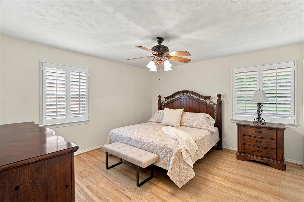 Room featuring light wood-finish flooring, white plantation shutters, and a central ceiling fan with multi-light fixture