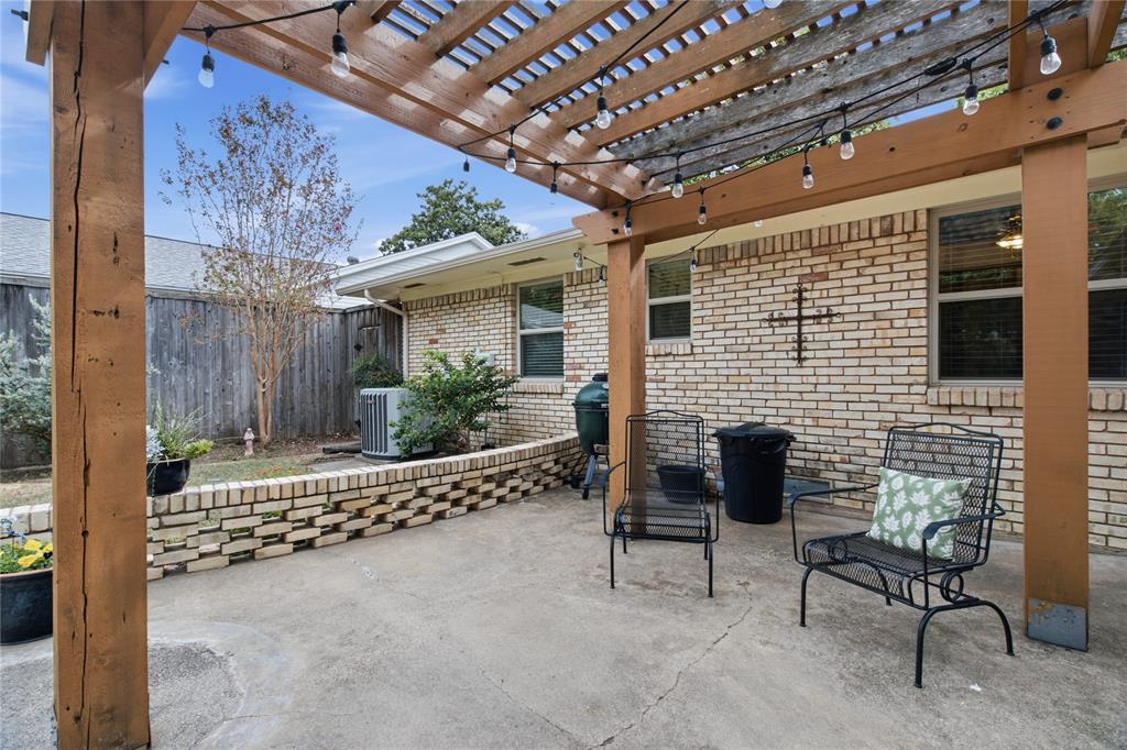 Concrete patio featuring a timber pergola, brick exterior wall, and low-profile decorative brick retaining wall