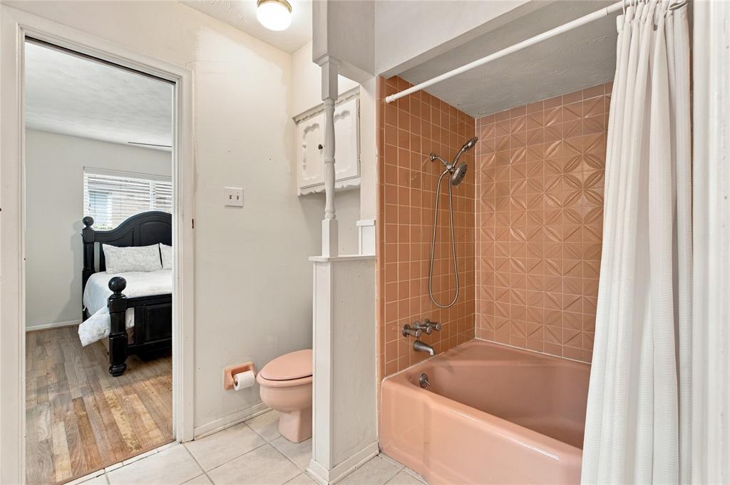 Bathroom featuring a tub with an integrated shower head and geometric-patterned tile surround, pink porcelain fixture, wall-mounted cabinetry, and tile flooring