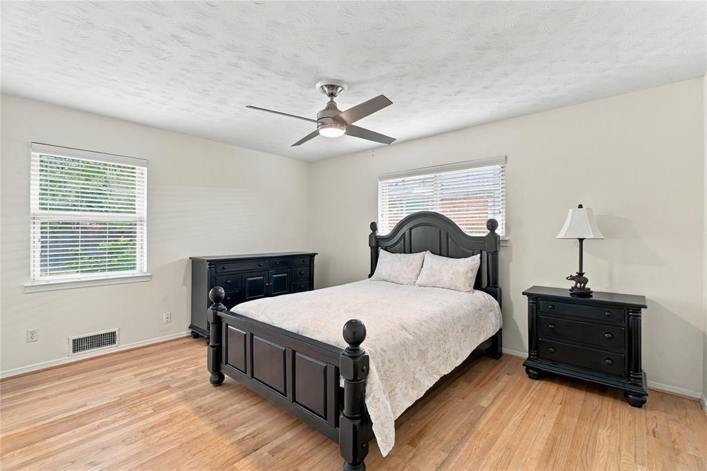 Room with light-toned wood-finish flooring, dual windows with blinds, and a central ceiling fan with integrated lighting