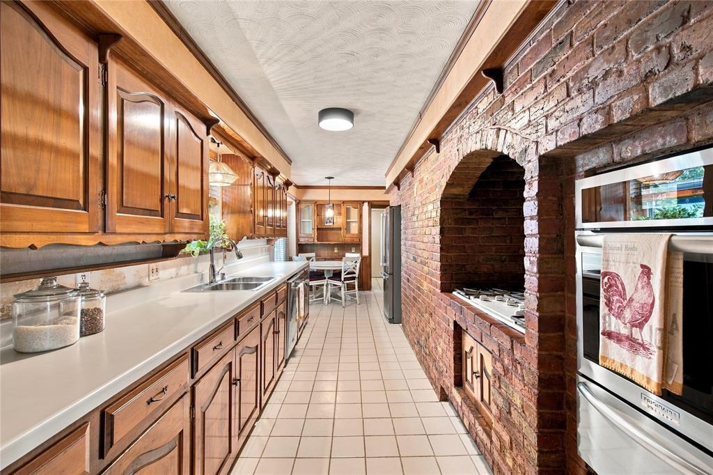 Galley kitchen featuring wood cabinetry, solid surface countertops, exposed brick wall with arched brick cooktop surround, and ceramic tile flooring Galley kitchen featuring wood cabinetry, solid surface countertops, exposed brick wall with arched brick cooktop surround, and ceramic tile flooring