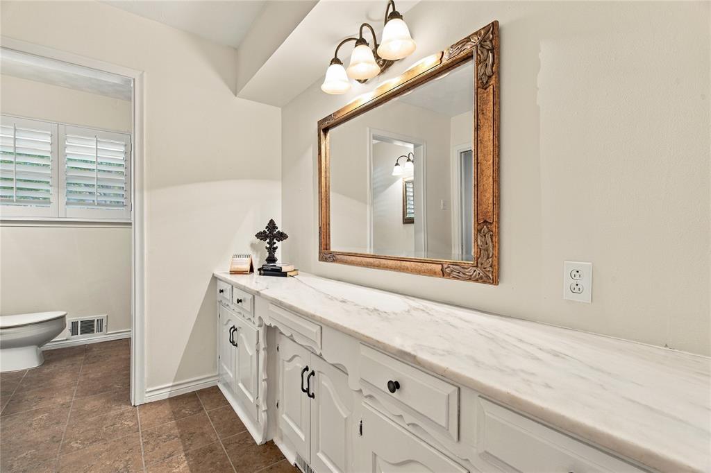 Extended vanity featuring white cabinetry, a stone-surfaced countertop, a decorative framed mirror, and three-light wall-mounted fixture