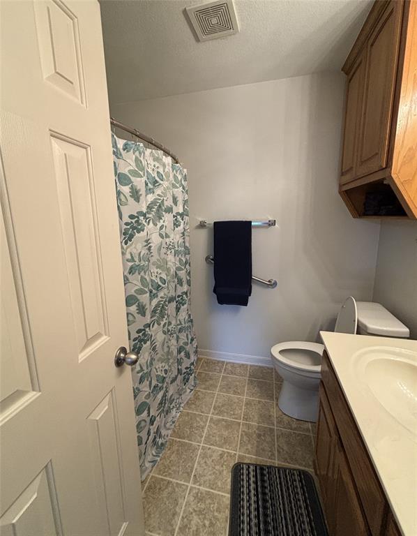 Bathroom featuring a vanity with wood-finish cabinetry, integrated sink, tiled flooring, wall-mounted grab bars, and an elevated storage cabinet