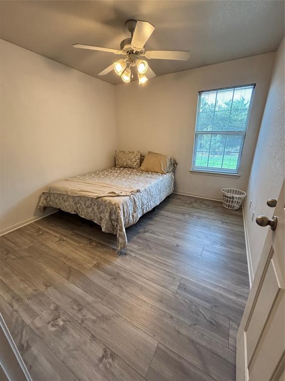 Wood-finish flooring, single-hung window with a grid pattern, and a ceiling fan with integrated lighting