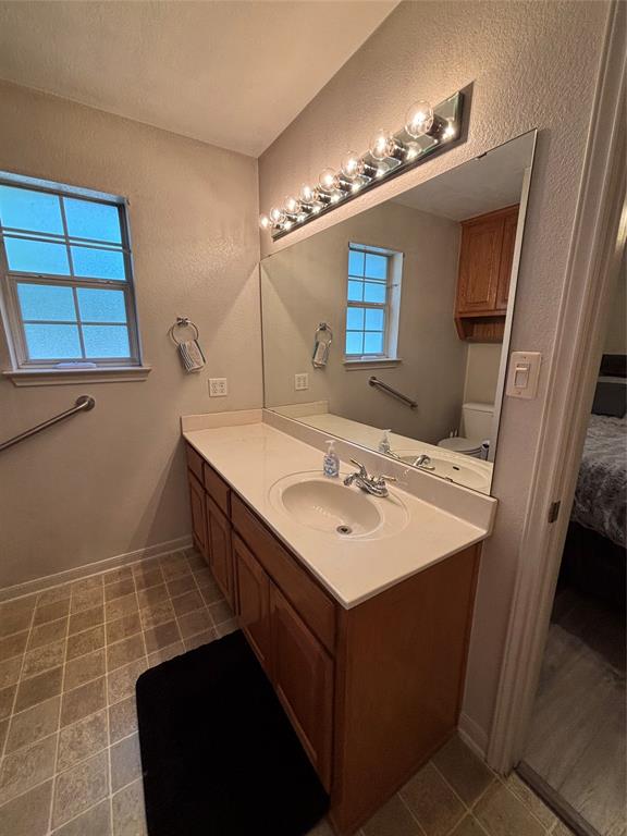 Primary bathroom vanity featuring wood-finish cabinetry, a solid-surface countertop with an integrated basin, a full-width wall mirror, and multi-bulb lighting.