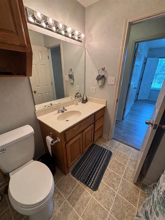 Vanity with wood-finish cabinetry, solid-surface countertop, integrated basin, and multi-bulb vanity lighting