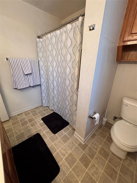 Primary bathroom featuring tile flooring, a built-in wood-finish upper cabinet, a combination tub and shower with a metal grab bar, and a wall-mounted towel bar Primary bathroom featuring tile flooring, a built-in wood-finish upper cabinet, a combination tub and shower with a metal grab bar, and a wall-mounted towel bar