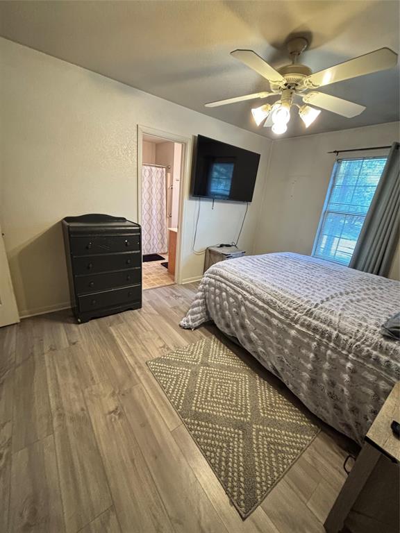 Primary bedroom featuring wood-finish flooring, a ceiling fan with integrated lighting, and a window with neutral drapery