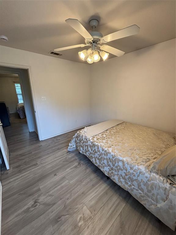 Room featuring wood-finish flooring, a white ceiling fan with integrated four-light fixture, and neutral wall paint