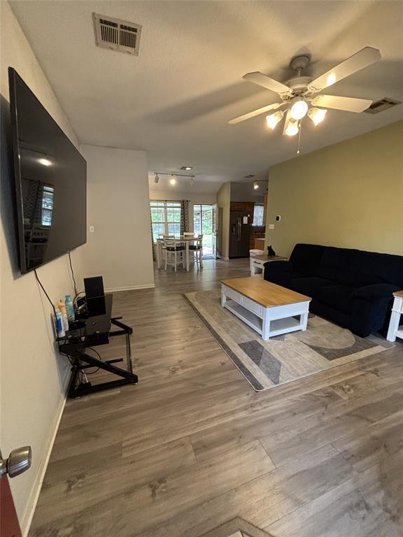 Open-concept interior featuring wood-finish flooring, a multi-blade ceiling fan with integrated lighting, and track lighting fixtures Open-concept interior featuring wood-finish flooring, a multi-blade ceiling fan with integrated lighting, and track lighting fixtures