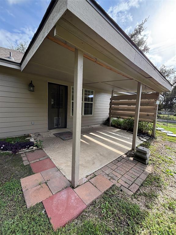 Covered patio featuring a concrete slab foundation, wood-post supports, privacy screen, and multi-colored paver border