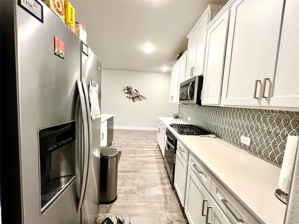 Kitchen with stainless steel appliances, white cabinetry, light wood-type flooring, and tasteful backsplash