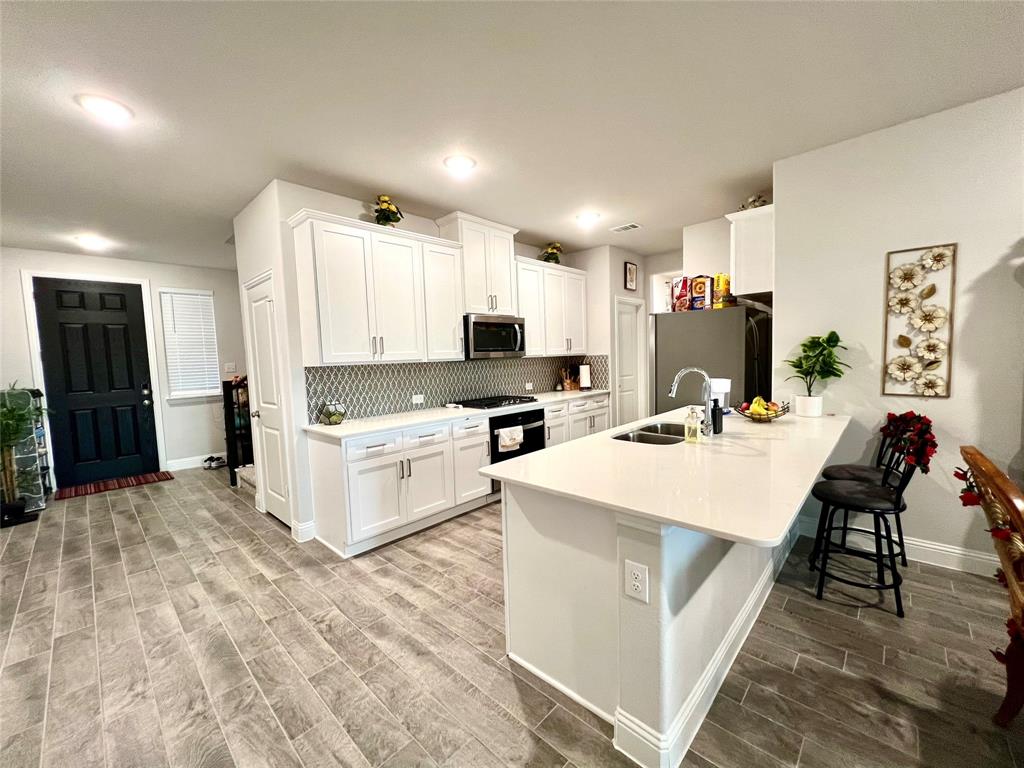 Kitchen with sink, light hardwood / wood-style flooring, white cabinetry, appliances with stainless steel finishes, and a kitchen bar